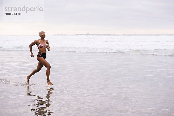Frau im Bikini joggen am Strand