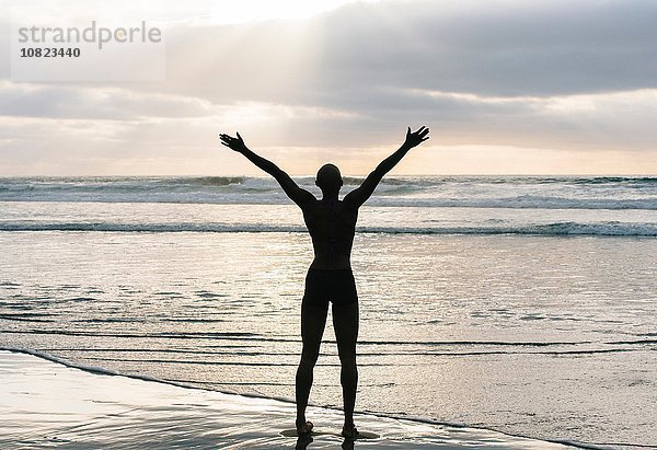 Silhouette der Person  die die Arme am Strand hebt