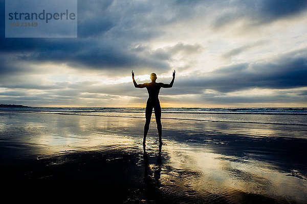 Silhouette der Person  die die Arme am Strand hebt