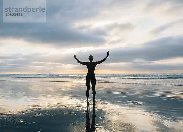 Silhouette der Person  die die Arme am Strand hebt