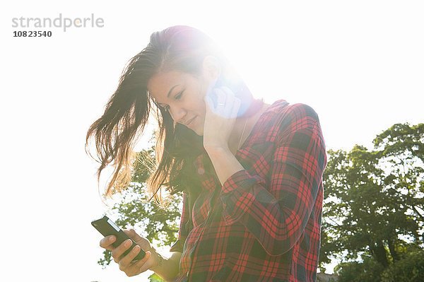 Junge Frau liest Smartphone-Texte gegen den sonnigen Himmel