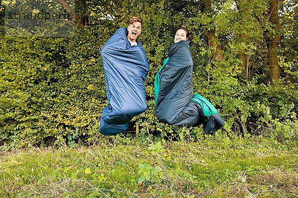 Junges Paar springt in der Luft in den Schlafsäcken
