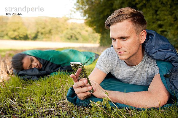 Junger Mann liegt Schlafsack SMS auf Smartphone im Feld