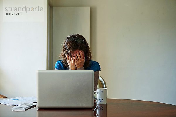 Junge Frau am Tisch sitzend mit Laptop  sieht gestresst aus