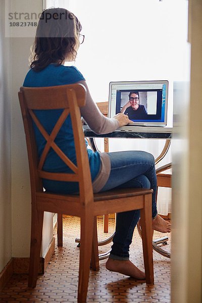 Junge Frau am Tisch sitzend  mit Laptop  auf Videogespräch mit reifer Frau  Rückansicht