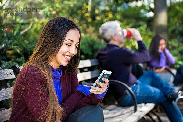 Junge Frau sitzt auf der Parkbank und liest Smartphone-Texte.