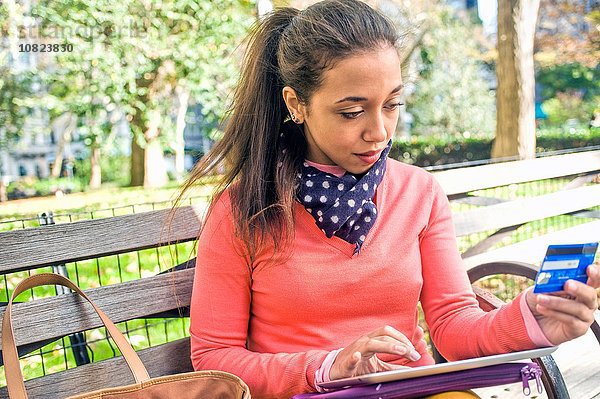 Junge Frau auf Parkbank sitzend mit Kreditkarte und digitalem Tablett
