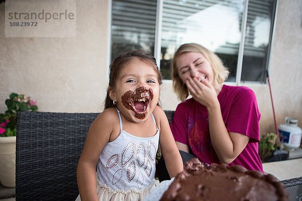 Junges Mädchen  Schokoladenkuchen auf dem Gesicht  sitzend mit Familienmitglied  lachend
