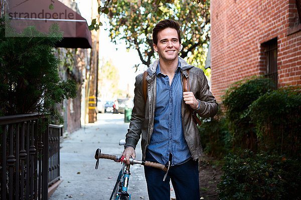 Glücklicher junger Mann schlendert mit Fahrrad auf dem Bürgersteig