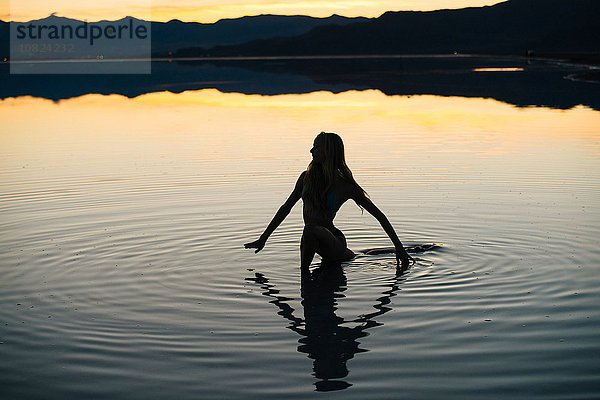 Silhouette einer jungen Frau  die bei Sonnenuntergang im See watet  Bonneville Salt Flats  Utah  USA