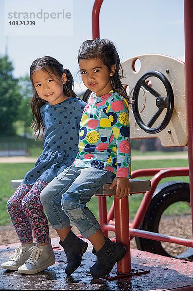 Porträt von zwei Mädchen  die auf dem Klettergerüst des Spielplatzes sitzen