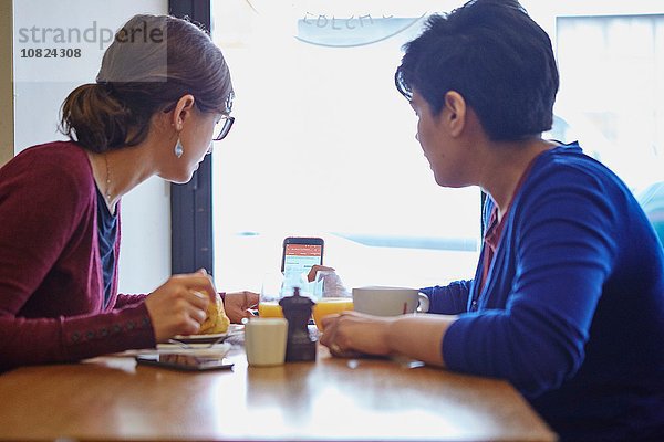 Zwei Frauen lesen Smartphone-Text im Restaurant