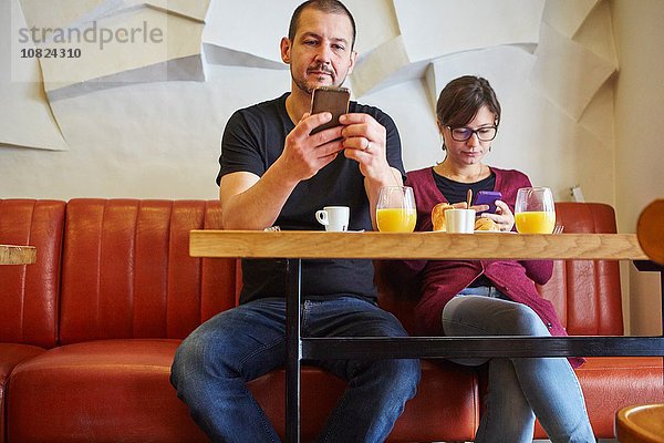 Mittleres erwachsenes Paar beim Lesen von Smartphone-Texten im Restaurant