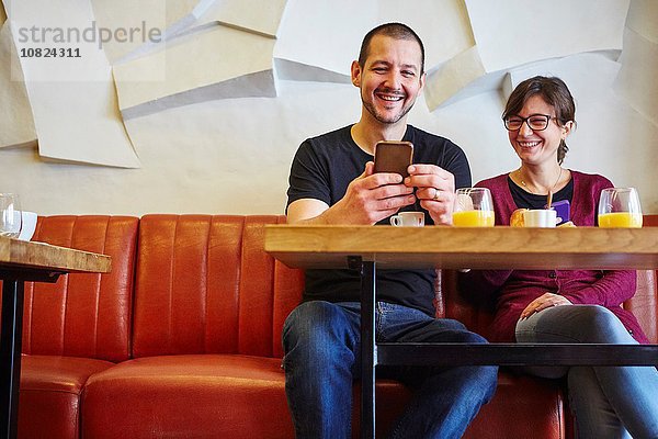 Mittleres erwachsenes Paar beim Lesen von Smartphone-Texten im Restaurant