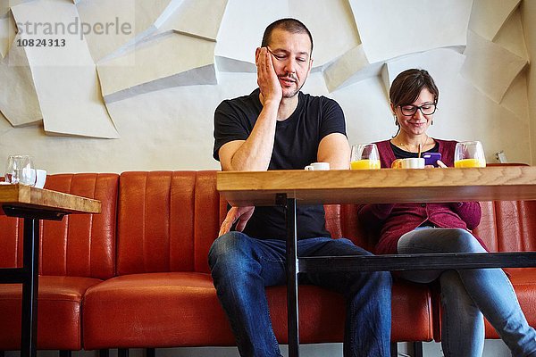 Gelangweilter Mann mit Freundin beim Lesen von Smartphone-Text im Restaurant