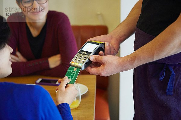 Abgeschnittene Aufnahme einer Frau  die die Karte in den Kreditkartenautomaten im Restaurant einsteckt.