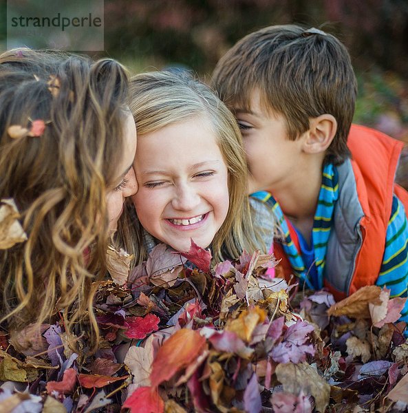 Kinder liegen auf Herbstblättern im Garten