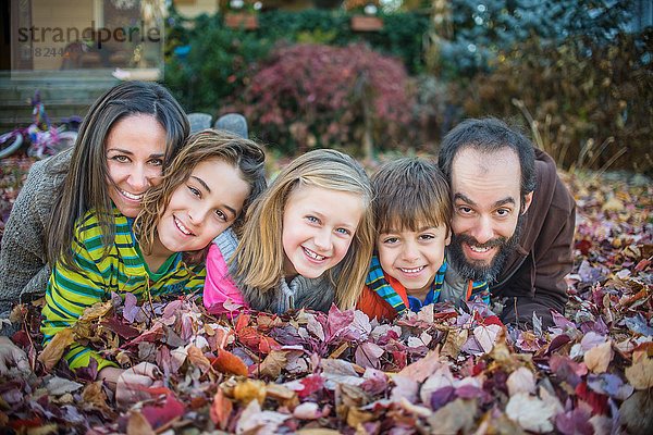 Familie auf Herbstlaub im Garten liegend