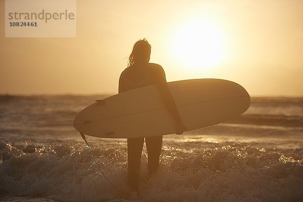 Silhouette eines jungen  männlichen Surfers mit Surfbrett im Meer  Devon  England  UK