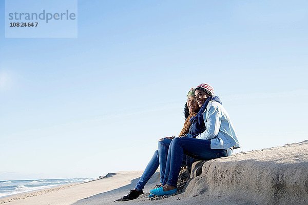 Zwei Freunde  die am Strand sitzen und auf die Aussicht schauen.