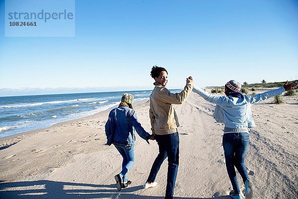 Drei Freunde  die am Strand spazieren gehen  Händchen haltend  Rückansicht