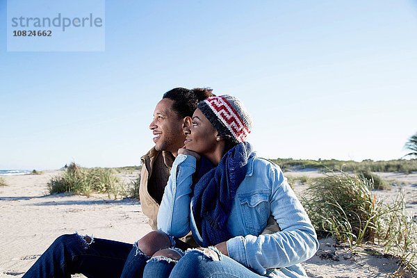 Junges Paar am Strand sitzend  mit Blick auf die Aussicht