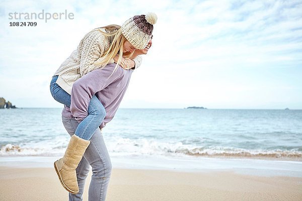 Junger Mann gibt Freundin ein Huckepack am Strand  Constantine Bay  Cornwall  UK