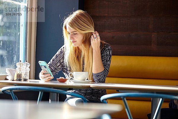 Junge Frau allein im Café beim Lesen von Smartphone-Texten