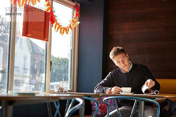 Junger Mann allein im Café  Kaffee trinken und Magazin lesen