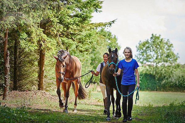 Durchgehende Vorderansicht des Mädchens und der reifen Frau  die das Bleiseil hält und mit Pferden geht  die lächelnd in die Kamera schauen.