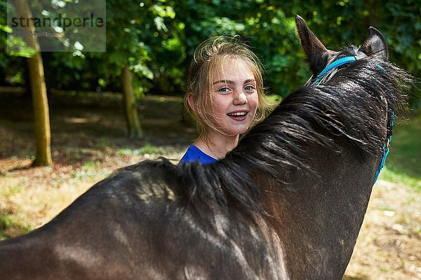 Kopf und Schultern eines Mädchens mit Pferd  das lächelnd in die Kamera schaut.