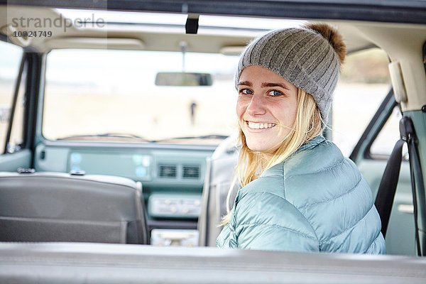 Porträt einer jungen Frau im Auto am Strand mit Strickmütze