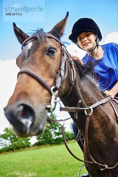 Niedriger Blickwinkel des Mädchens auf dem Rücken eines Pferdes mit lächelndem Reiterhut