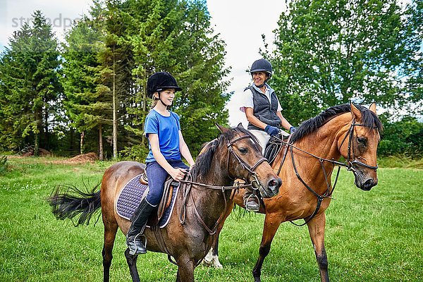 Reife Frau und Mädchen zu Pferd mit lächelndem Reiterhut