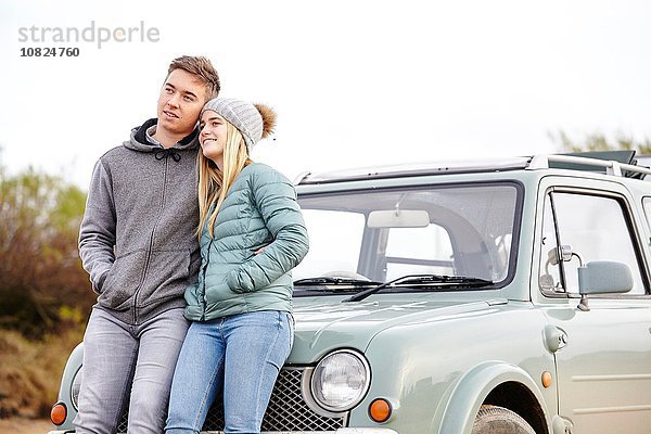 Romantisches junges Paar  das sich am Strand gegen das Auto lehnt.