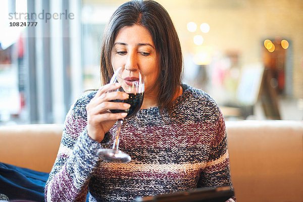 Reife Frau trinkt rot und liest digitales Tablett in der Weinstube
