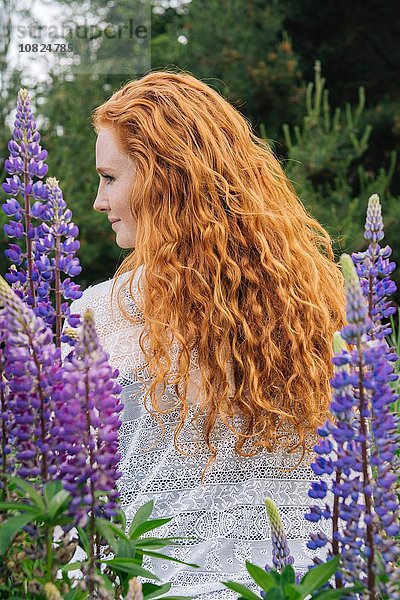 Rückansicht Porträt einer jungen Frau mit langen roten Haaren unter lila Wildblumen