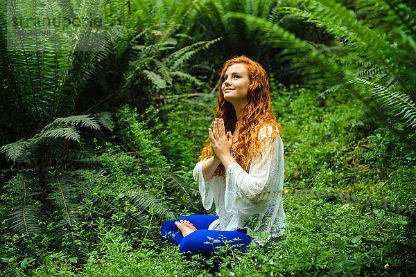 Junge Frau im Wald praktiziert Yoga in Lotusstellung
