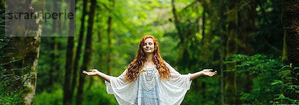 Panoramabild einer jungen Frau  die mit offenen Armen im Wald meditiert.