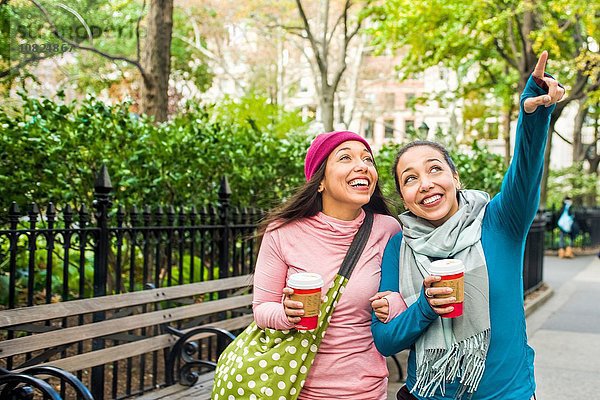 Zwillinge gehen mit Kaffee spazieren und zeigen in den Park.