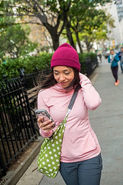 Junge Frau beim Gehen und mit dem Smartphone im Park