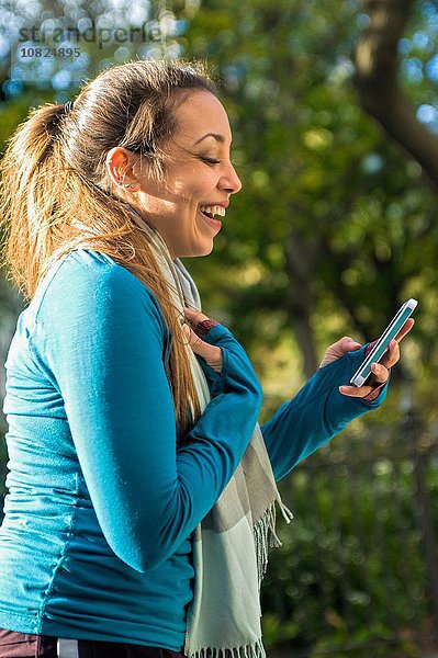 Junge Frau lächelt bei Nachricht auf dem Smartphone im Park