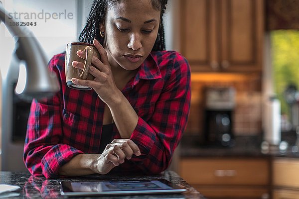 Mittlere erwachsene Frau am Küchenarbeitsplatz mit digitalem Tablett