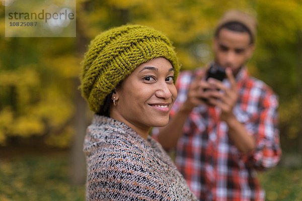 Porträt einer mittleren erwachsenen Frau  die von ihrem Freund im Herbstwald fotografiert wird.