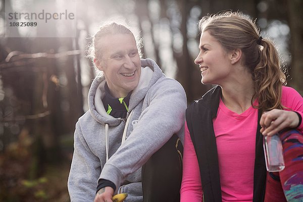 Paar in Sportkleidung hält Wasserflasche sitzend von Angesicht zu Angesicht lächelnd