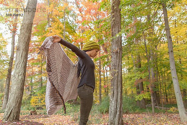 Mittlere erwachsene Frau hält ihr Tuch im Herbstwald hoch.