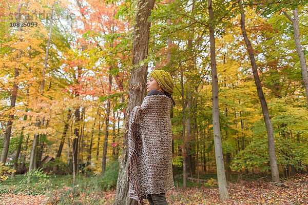 Mittlere erwachsene Frau in Tuch gewickelt im Herbstwald stehend