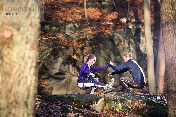 Seitenansicht des Paares auf Felsen im Wald von Angesicht zu Angesicht  Händchen haltend  hockend auf einem Bein balancierend