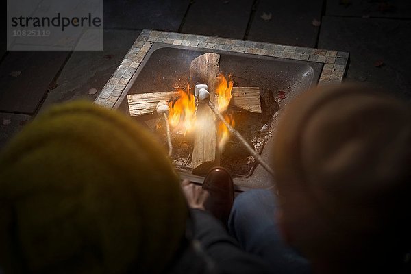 Rückansicht des Paares mit Strickmützen auf dem Lagerfeuer in der Nacht.