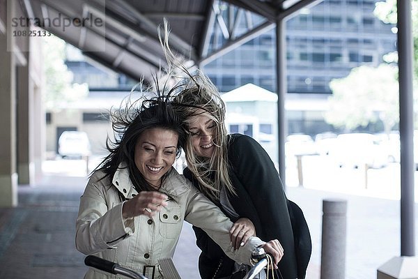 Zwei Freundinnen mit fliegendem Haar lachend auf dem Fahrrad in der Stadt